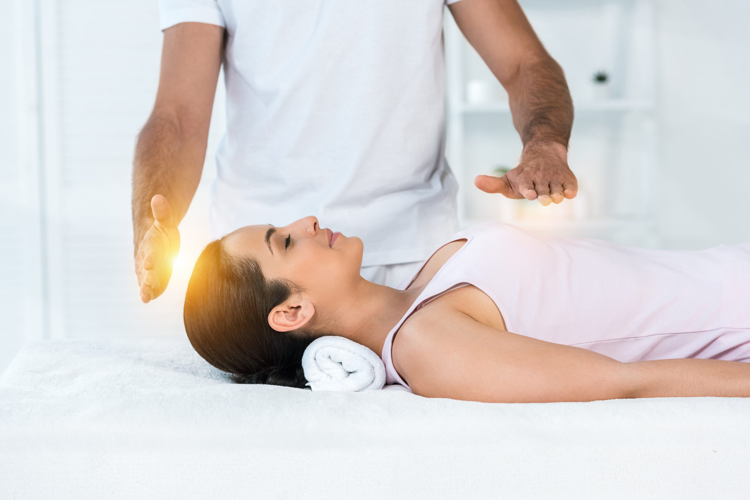 cropped view of healer putting hands above body of attractive woman with closed eyes lying on massage table